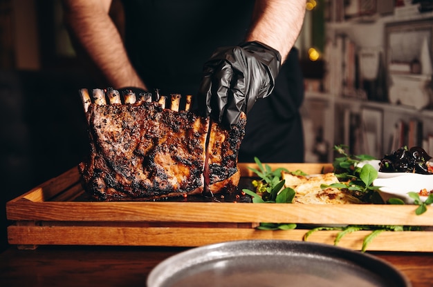 Chef cutting grilled roasted rack of lamb on wooden board