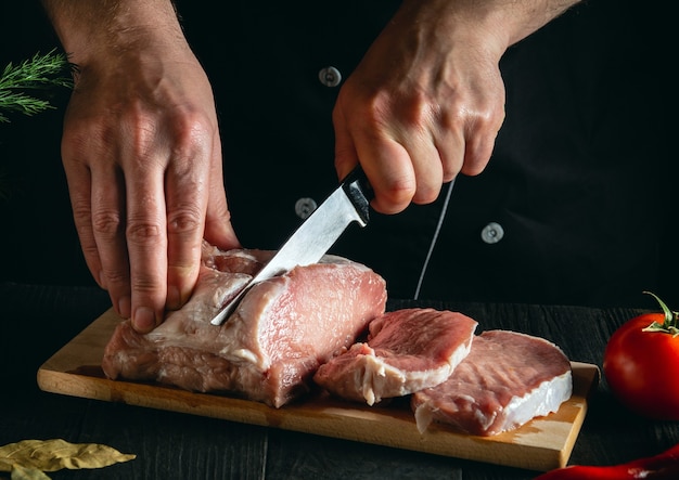 Шеф-повар режет мясо ножом на кухне, готовит пищу Овощи и специи на кухонном столе