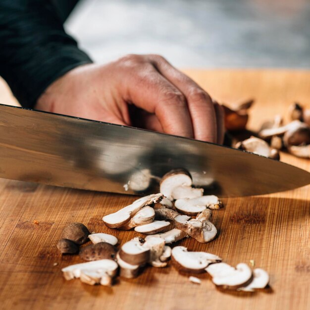 Chef Cutting Shiitake Mushrooms with Knife on a Wooden Cutting Board