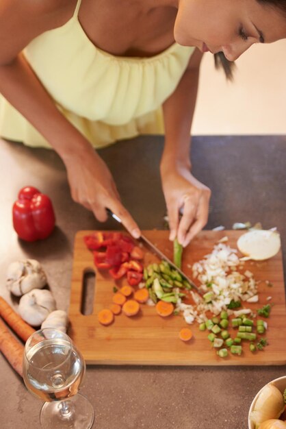 Foto cuoco cibo e salute con donna in cucina di casa per preparare il pasto per la dieta o la nutrizione dall'alto cucina nutrizionista o vegano e persona che taglia verdure verdi con un coltello in appartamento