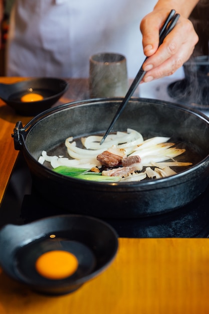 Шеф-повар жареный лук, лук-шалот и грибы в горячий горшок Sukiyaki.