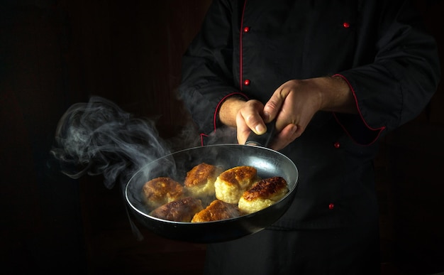 Foto lo chef frigge le ciambelle in una padella il concetto di preparazione di un piatto nazionale polacco nella cucina di un ristorante spazio nero per la ricetta o il menu