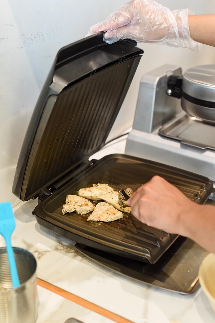 Photo 電気グリルでバターで鶏肉を揚げるシェフ