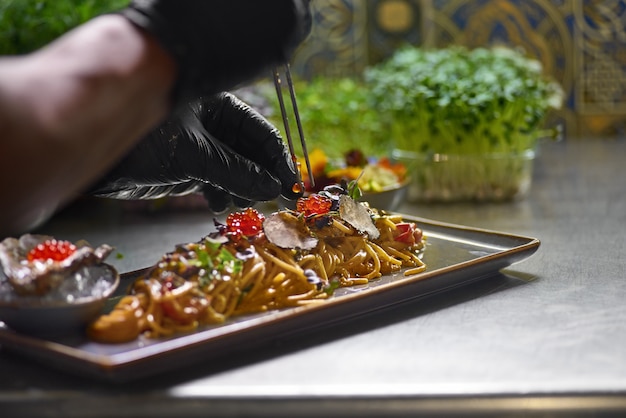 The chef garnishes with red caviar a seafood spaghetti dish, Selective focus.