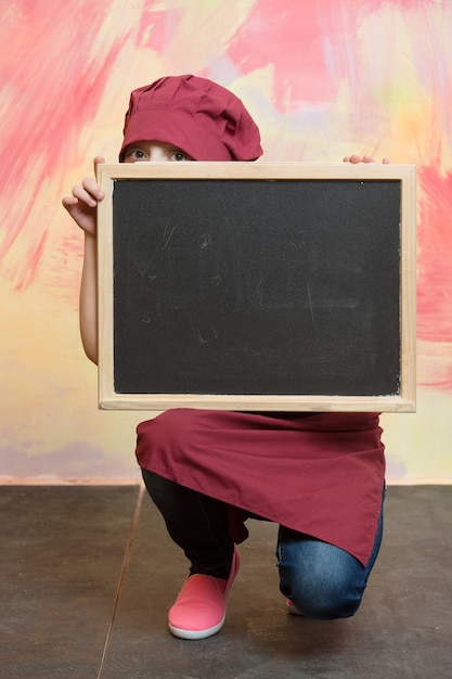 Chef girl or cook child in red hat on colorful background behind board, copy space, cooking and food