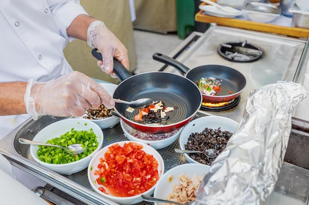 사진 요리사 가 장갑 을 쓴 손 으로 채소 와 다른 재료 들 을 김판 에 있는 가스 스토브 에서 조리 한다