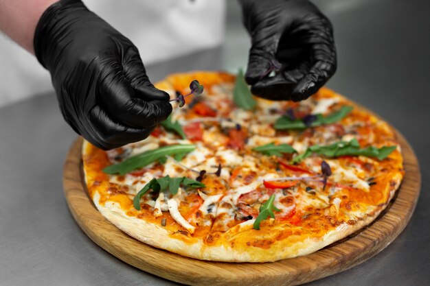 Chef in gloves decorates pizza with greens