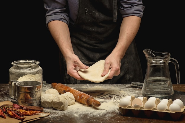 Le mani dello chef stanno preparando un impasto sul tavolo di legno. colpo basso