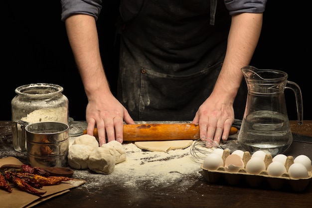 Chef hands are rolling a dough on wooden table. low key shot