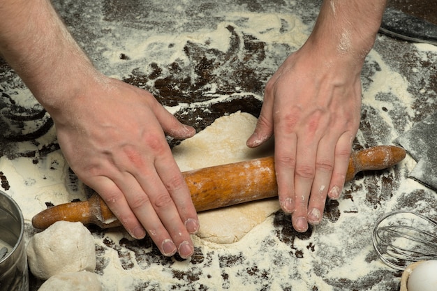 Chef hands are rolling a dough on wooden table