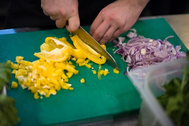 料理やサラダのために新鮮でおいしい野菜を切るシェフの手