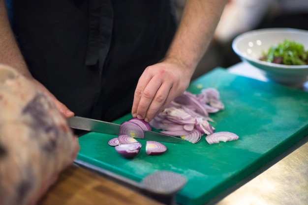 Mani dello chef che tagliano la cipolla con il coltello. preparazione per la cottura. alimentazione sana e stile di vita.