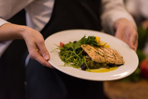 Chef hands holding fried Salmon fish fillet with vegetables for dinner in a restaurant kitchen