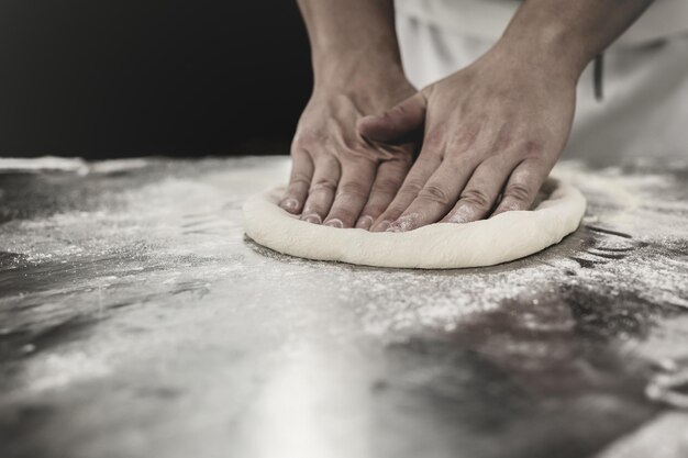 Foto le mani del cuoco che impastano l'impasto per la preparazione della pizza