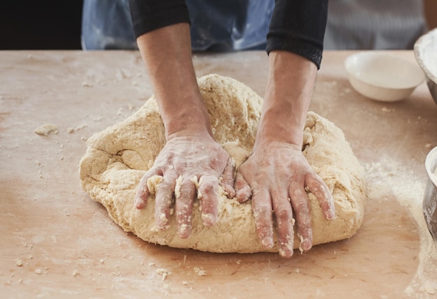 Руки шеф-повара замешивают тесто на деревянном кухонном столе. Подготовка к выпечке