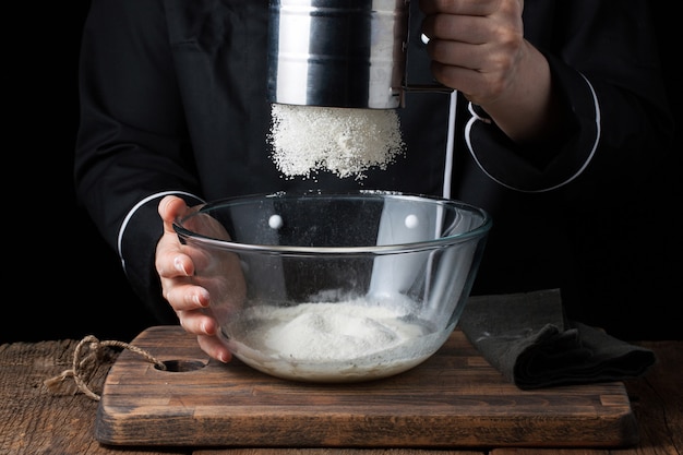 Chef hands pouring flour powder on raw dough.