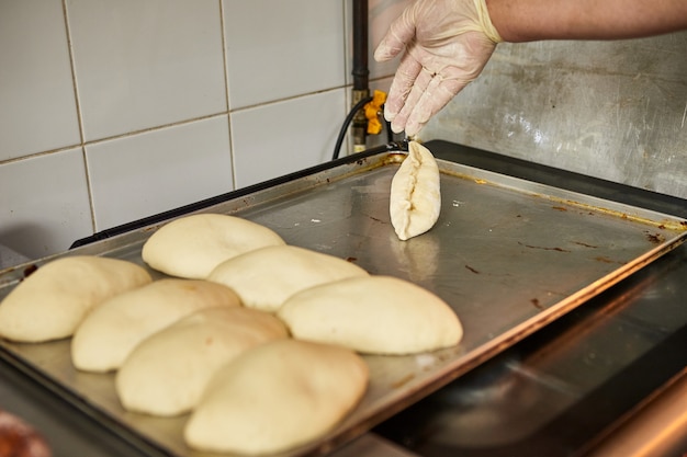 Chef hands prepares apple pies in the restaurant kitchen. The process of making sweet buns. Raw dough for baking in the oven.