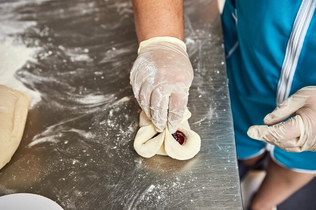 Chef hands prepares cherry pies in the restaurant kitchen. The process of making sweet buns. Raw dough for baking in the oven.