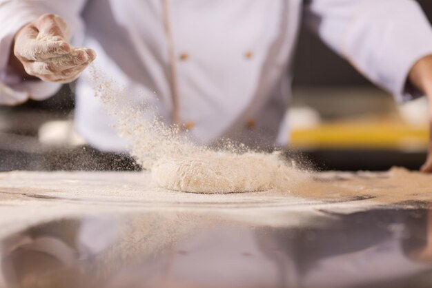 Chef hands preparing dough for pizza on sprinkled with flour\
table closeup