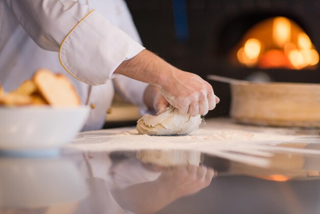 chef hands preparing dough for pizza on sprinkled with flour table closeup