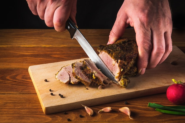 Chef hands slicing baked beef steak with knife on wood cutting desk. Top view food preparation process concept.