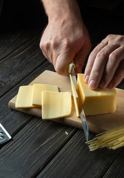キッチンでサンドイッチイタリアのピザや軽食用の木の板にチーズを切るナイフを持つシェフの手調理の準備健康的な食事とライフスタイル食品のコンセプト