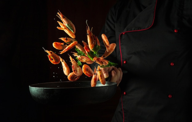 The chef in his hand holds a frying pan with frozen shrimp and parsley Isolated on a dark background Sea food or seafood recipes and restaurant and home cooking