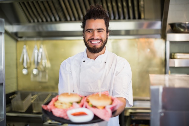 Hamburger della tenuta del cuoco unico in piatto alla cucina commerciale