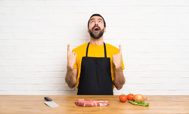 Chef holding in a cuisine surprised and pointing up