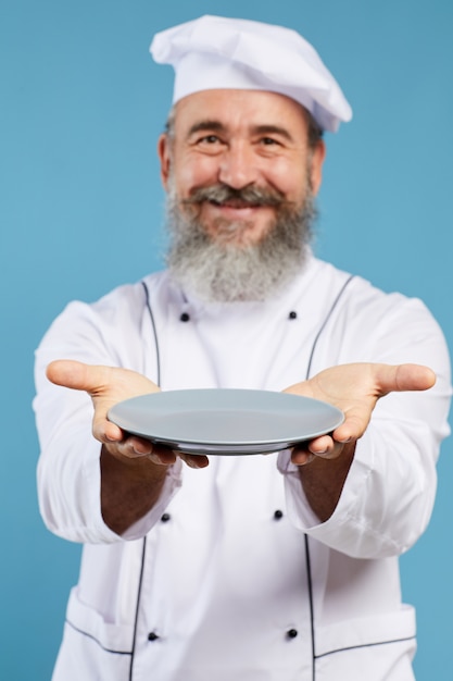 Шеф-повар держит пустую тарелку на синем