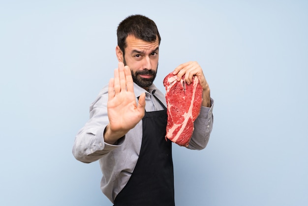 Photo chef holding a raw meat making stop gesture and disappointed