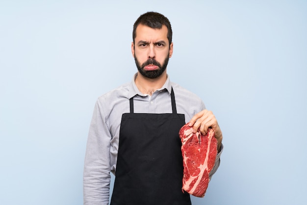 Photo chef holding a raw meat with sad and depressed expression