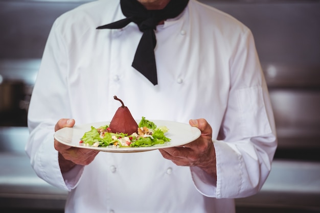 Шеф-повар держит и показывает блюдо с салатом