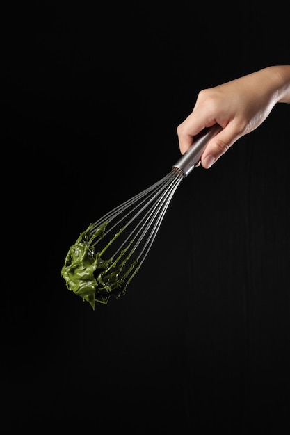 Chef holding wire whisk and green tea cream on black background
