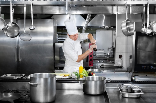 Chef in hotel or restaurant kitchen cooking he is seasoning dishes