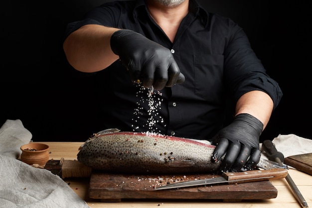 黒いシャツと黒いラテックス手袋のシェフが鮭の切り身を準備します