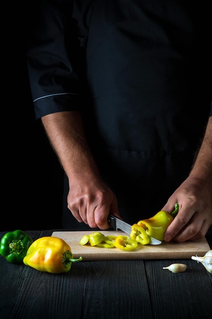 The chef is cutting bell peppers for salad in the restaurant kitchen. Close-up of a cook hands while working.