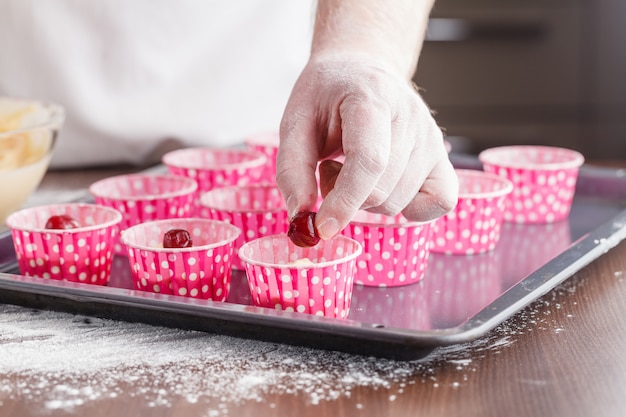 Chef is decorating delicious organic muffins. cherry cup cakes in natural setting.