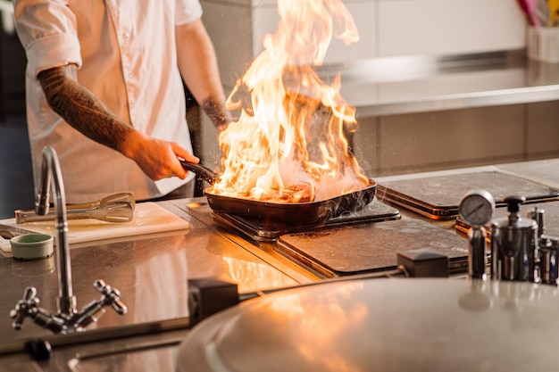 Chef is friing a steak with a fire at the restaurant kitchen