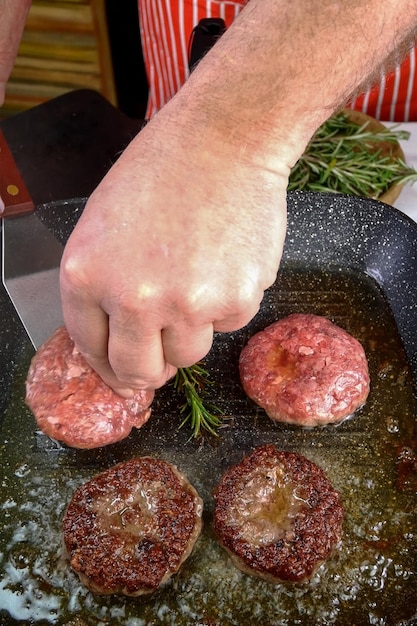 Chef is frying beef meat cutlets for burger in grill pan with oil Cook preparing meat dish on domestic kitchen at home