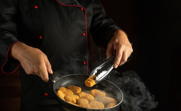 Шеф-повар жарит хрустящие нагиты на сковородке Концепция вкусного завтрака для отеля или ресторана Место для рецепта или меню на черном фоне