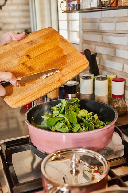 Chef is frying sorrel in frying pan in oil on gas stove