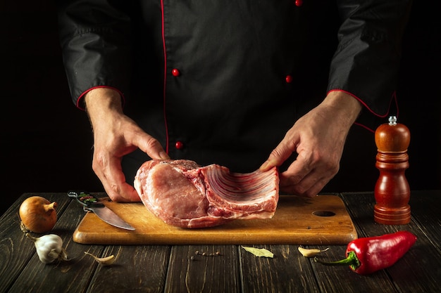 Lo chef tiene in mano un pezzo di carne cruda con un osso in cucina