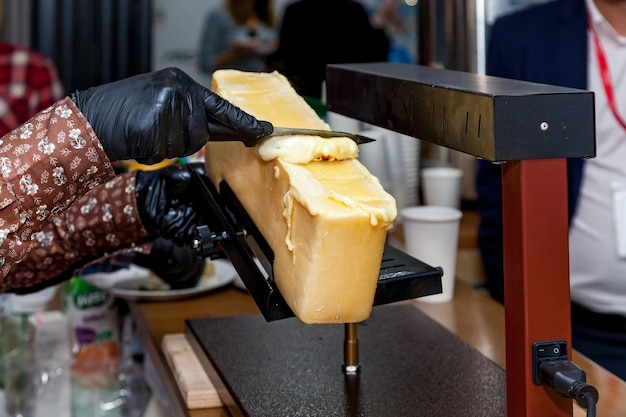 A chef is preparing a dish with raclette using a special instrument for cheese melting.