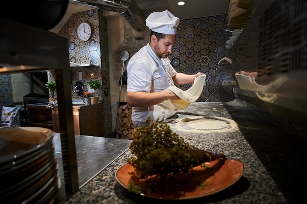 Chef is working on nicely decorated kitchen, preparing pastry for pizza.