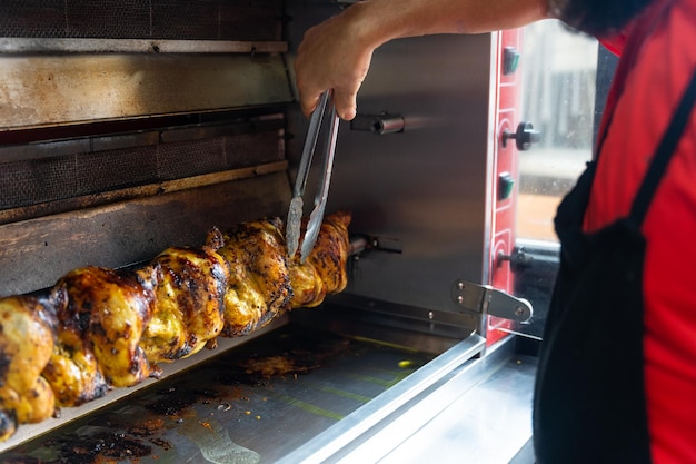 Chef of the kebab restaurant with a metal tool controlling the\
chicken grill