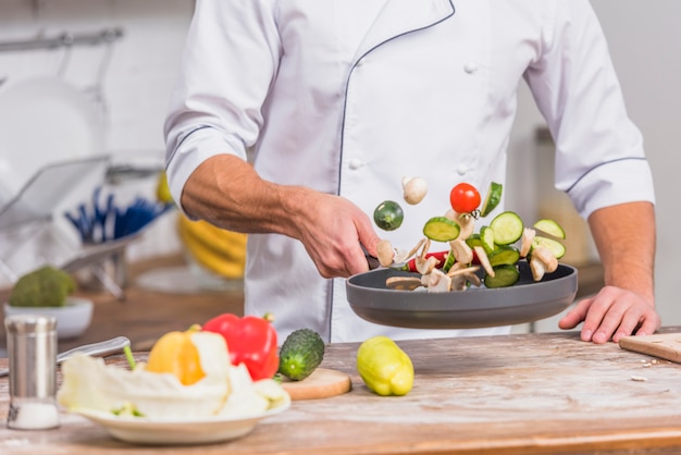 Chef in kitchen cooking with vegetables