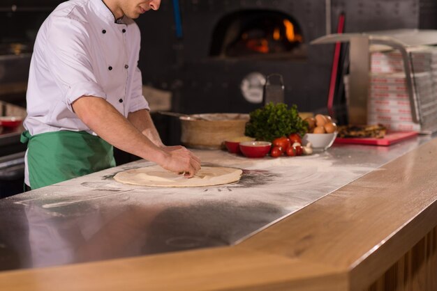 chef-kok bereidt deeg voor pizza rollen met handen op bestrooid met bloem tafel