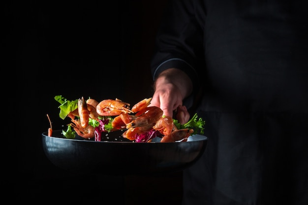 Chef-kok bereidt garnalen met kruiden. Koken zeevruchten, gezond vegetarisch eten en eten op een donkere achtergrond. Gratis advertentieruimte