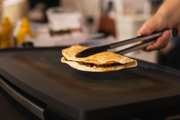 Foto chef-kok bereidt verse quesadilla op zwarte grill op de plaatselijke voedselmarkt